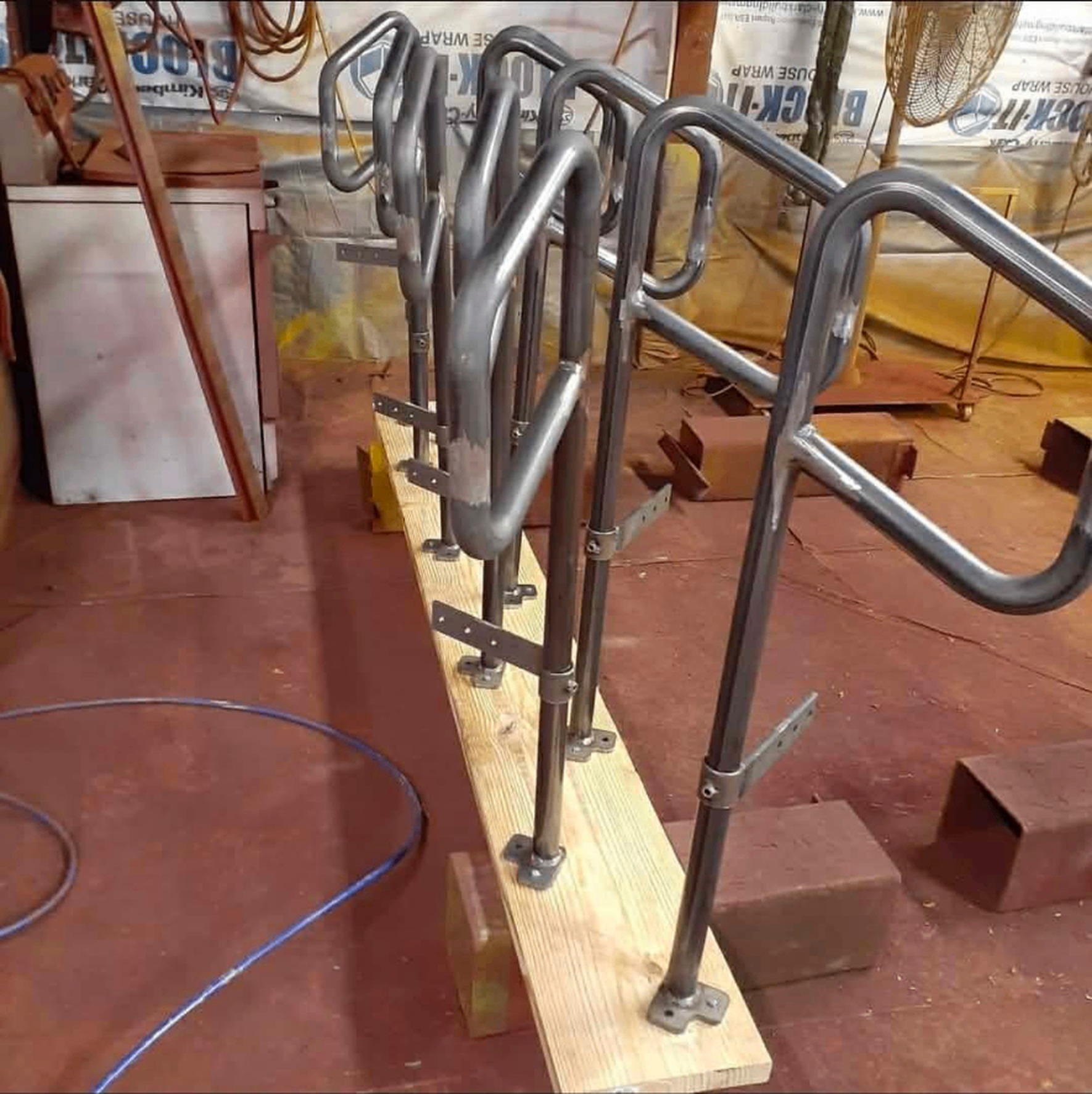Raw unpainted steel hand rails staged on a wood rack in the shop